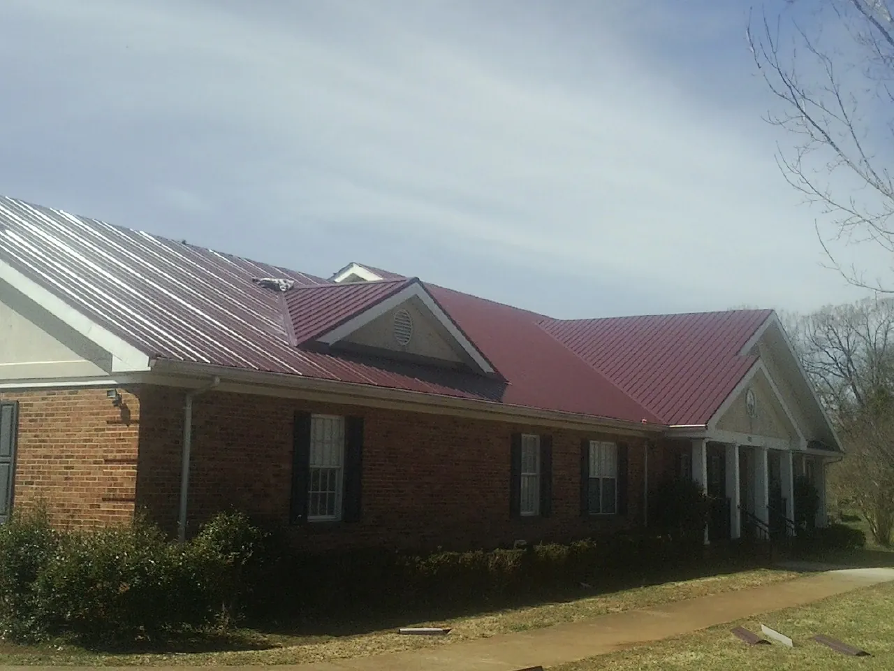 Red metal roof with gabled entries on a long brick building, from a Hail Damage Roof Repair job in Townley