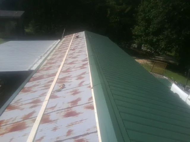 Old rusted panels beside newly installed green metal roofing — Wind Damage Roof Repair by Roofing Brothers in Townley