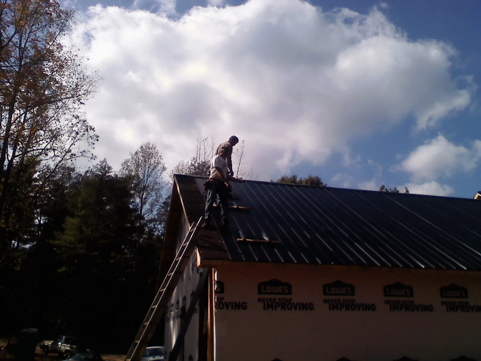 Roofer fastening dark metal panels high against a cloudy sky, from a Roof Inspection job in Townley