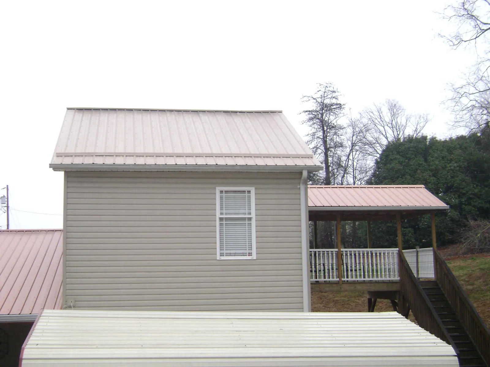 Tan metal roofs on a two story addition and attached porch, from a Roof Replacement job in Townley